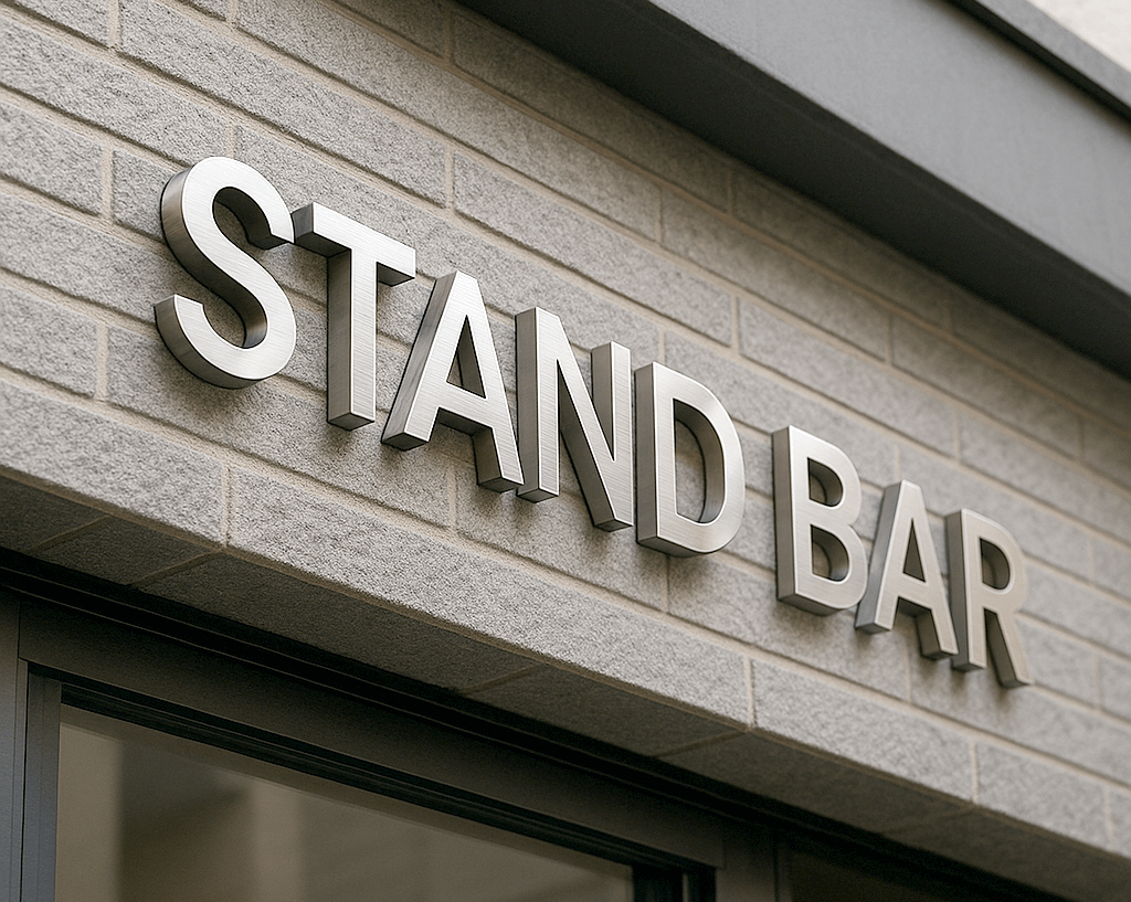 昼間のファサードにステンレス切り文字「STAND BAR」。ヘアラインが分かる斜め写真