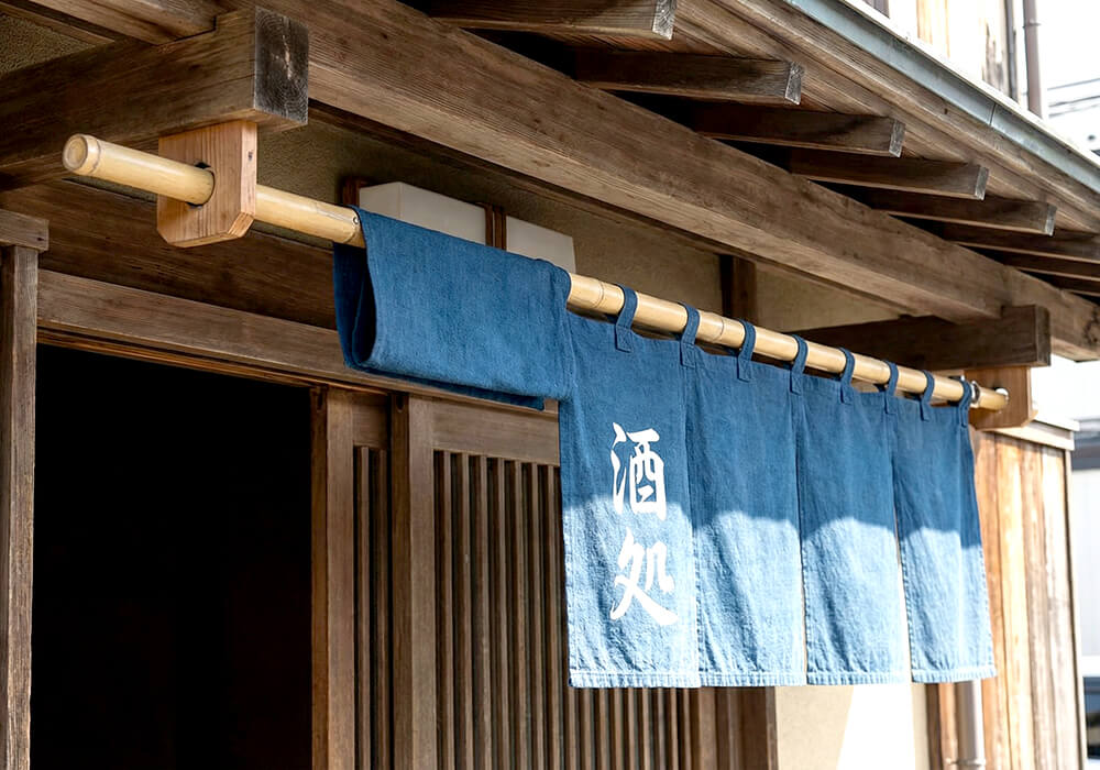 和風の居酒屋の軒先にパイプを通して設置された日除け幕の事例